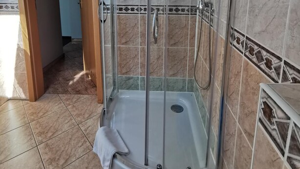 A bathroom with a shower enclosure, tiled walls, and a visible door leading to another room. - Hotel Zieliniec (Poznań)