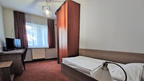 Ein Hotelzimmer mit Bett, Schreibtisch, Stuhl, Fernseher und einem Fenster mit Vorhängen.