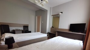 Ein Hotelzimmer mit zwei Betten, einem Fernseher, einem Schreibtisch und einem Spiegel.