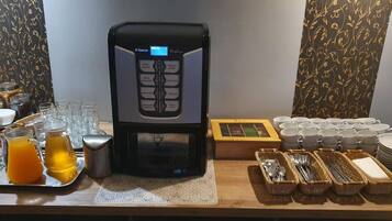 A coffee machine with multiple drink options, a tray with glasses and a pitcher of orange juice, and a table with utensils and plates.