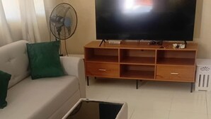 A living room with a sofa, a coffee table, a TV on a wooden stand, and a fan.