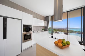 A modern kitchen with white cabinetry, stainless steel appliances, and a large island with a fruit basket. - Villa Fanta Sea (Koh Samui)