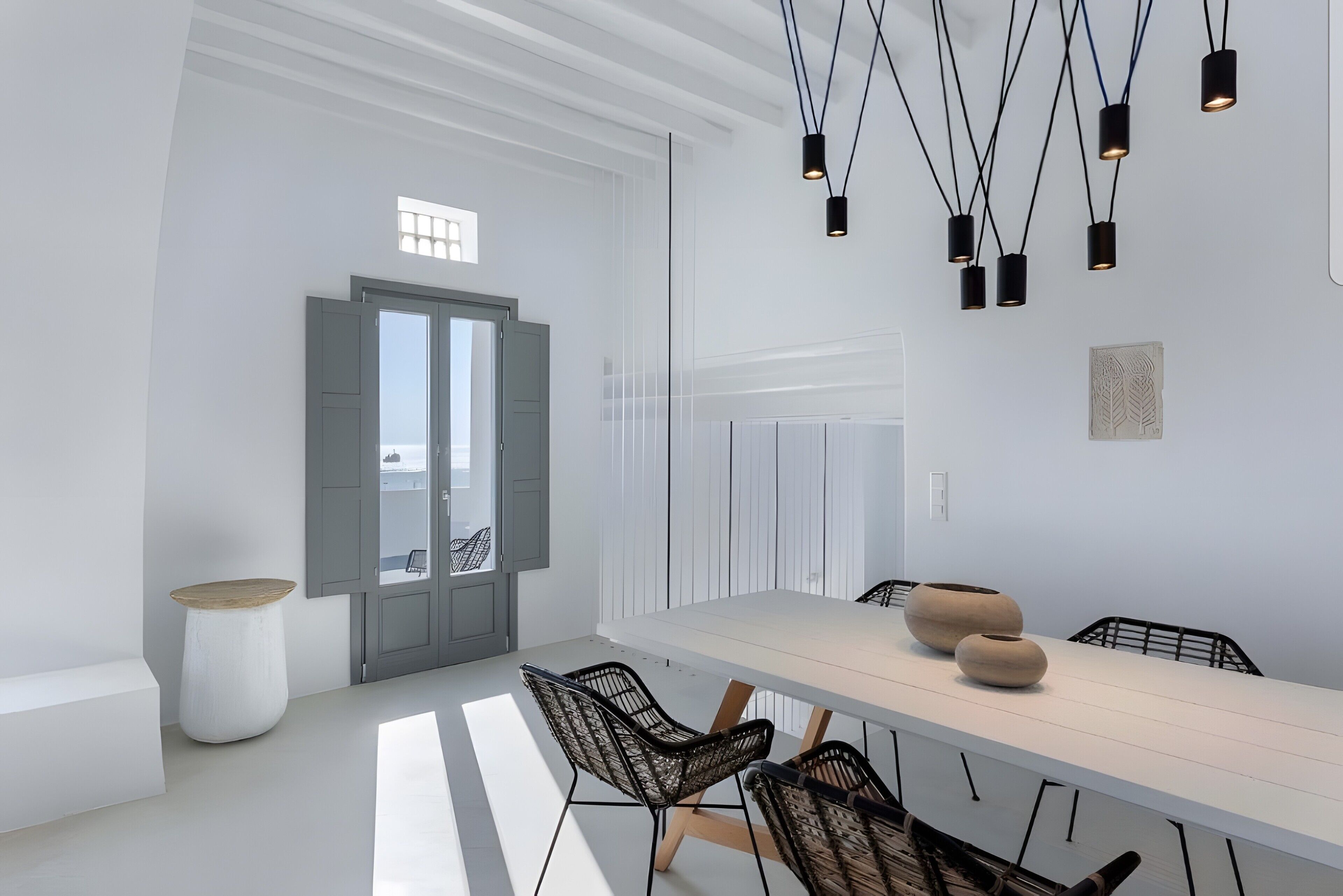 A modern dining area with a long table, black wicker chairs, and pendant lighting.