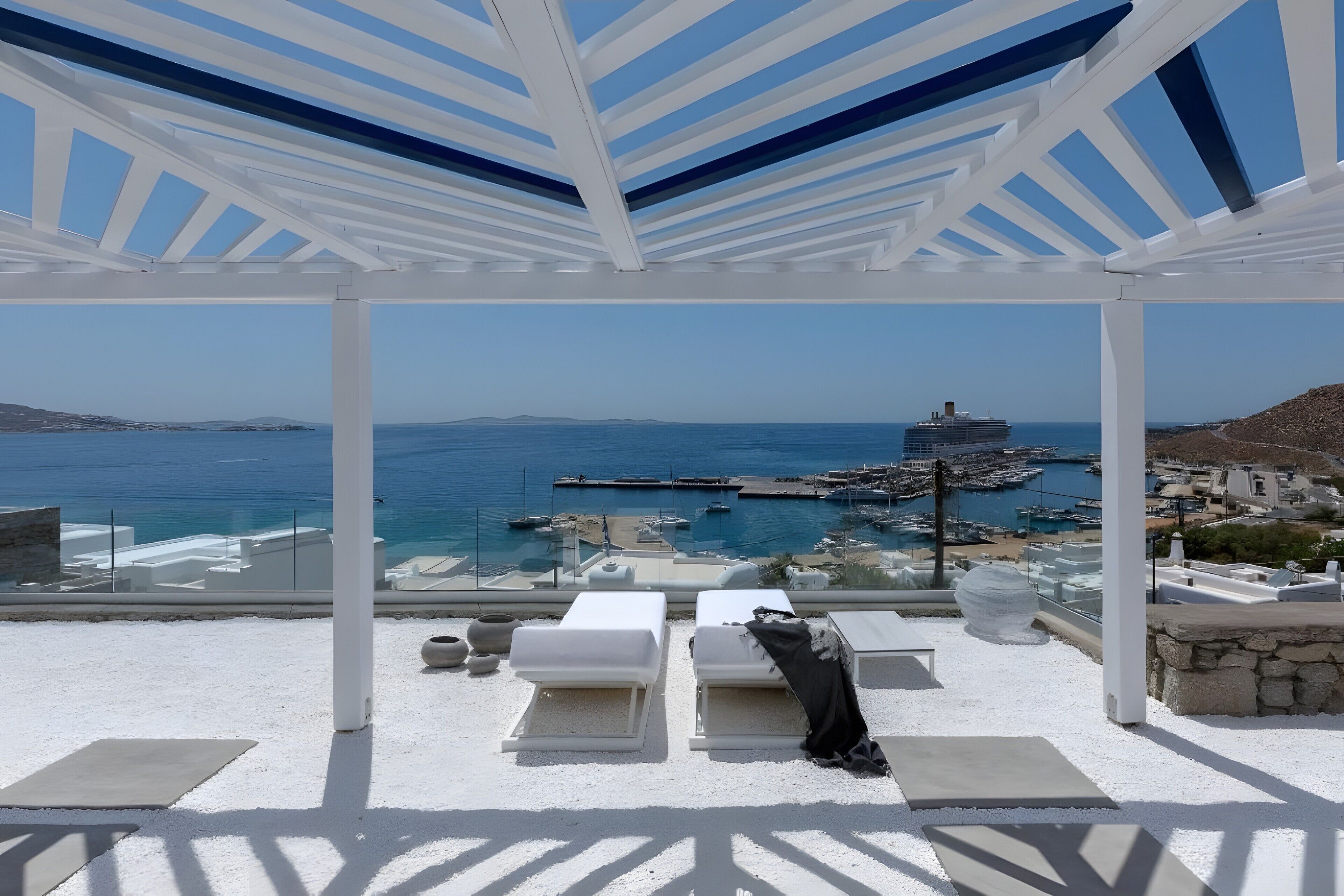A covered outdoor seating area with white lounge chairs and a view of the sea and port.