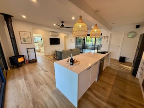 Cocina moderna con una isla central, suelo de madera, iluminación colgante y estufa empotrada.