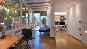 Um espaço de escritório moderno com escrivaninha de madeira, cadeira de escritório preta e parede de vidro com vista para o verde.