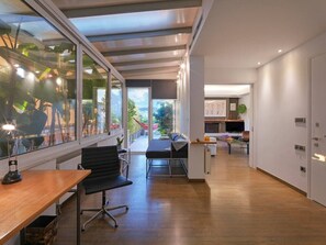 A modern office space with a wooden desk, black office chair, and a glass wall with a view of greenery. - AthensView Bird’s Eye Penthouse with Acropolis view (Athina)