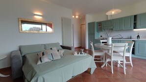 Un dormitorio con cama, mesita de noche, una silla y vista a la cocina.