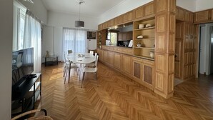A spacious living area with a dining table, chairs, and a kitchen with wooden cabinets. - AthensView Skyline: 5th fl, 2BR, Acropolis View (Athina)