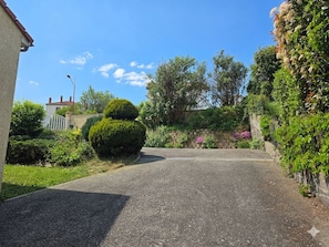 Une rue résidentielle avec une allée pavée, une haie bien entretenue et un ciel bleu dégagé.
