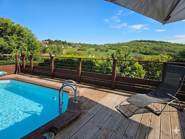 Une terrasse en bois avec une piscine, un fauteuil de relaxation et une vue sur un paysage verdoyant.