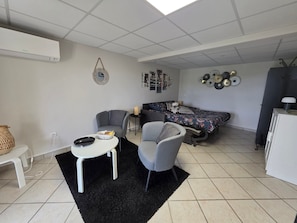 Un salon moderne comprenant un canapé, deux fauteuils, une petite table et un lit avec une literie à motifs.