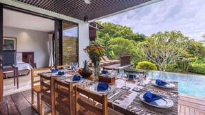 A dining area with a pool view, wooden furniture, and a ceiling fan. - O'hare Villa  (Jimbaran)