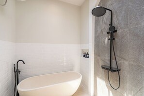Ein modernes Badezimmer mit einer freistehenden Badewanne, einer Duschbrause und einem wandmontierten Seifenspender.