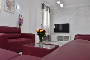 Ein modernes Wohnzimmer mit roten Sofas, einem Glastisch, einem Fernseher und einer dekorativen Vase mit Blumen.