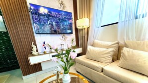 Ein modernes Wohnzimmer mit einer Couch, einem Couchtisch mit Dekorationsobjekten, einem Fernseher, der eine Stadtansicht zeigt, und einer Flagge an der Wand.