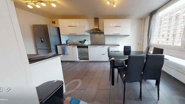 A modern kitchen with white cabinets, a stainless steel refrigerator, and a dining area with a table and chairs. - Private Room in a Shared Flat - Lyon 8 (Lyon)