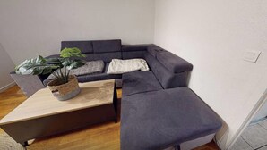 A corner room with a grey sofa, a small wooden table, and a potted plant. - Private Room in a Shared Flat - Lyon 8 (Lyon)