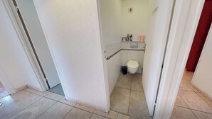 A narrow hallway leading to a bathroom with a toilet, a small shelf with toiletries, and a tiled floor. - Private Room in a Shared Flat - Lyon 8 (Lyon)