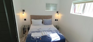 A bed with a floral bedspread, two pillows, and a folded towel on the bed. There are two bedside tables with lamps. - neo & Ruks Guest House (Cape Town)