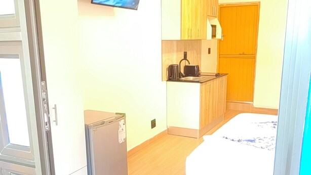 Ein kleines Zimmer mit einem Bett, einer Kochnische und einem an der Wand befestigten Fernseher.