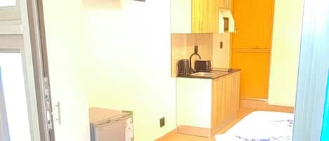 A compact room with a bed, a small kitchenette, and a television mounted on the wall.