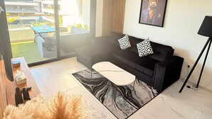 A modern living room with a black sofa, patterned cushions, a marble coffee table, and a large window offering a view of the outside. - Apartment TM lagoons Village 141 (Torrevieja)