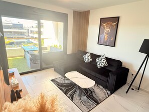 A modern living room with a black sofa, patterned cushions, a marble coffee table, and a large window offering a view of the outside. - Apartment TM lagoons Village 141 (Torrevieja)