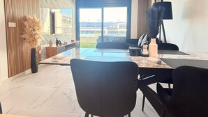 A modern living room with a large window, a flat-screen TV, a dining area with chairs, and a view of the cityscape. - Apartment TM lagoons Village 141 (Torrevieja)
