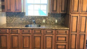 A kitchen with wooden cabinets, a granite countertop, a stainless steel sink, and a window above the sink.