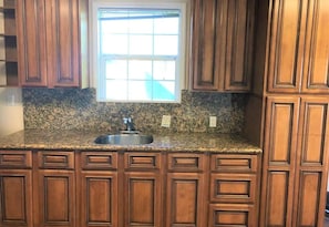 A kitchen with wooden cabinets, a granite countertop, a stainless steel sink, and a window above the sink. - Charming 2-bedroom house in beautiful San Mateo perfect for relaxing (San Mateo)