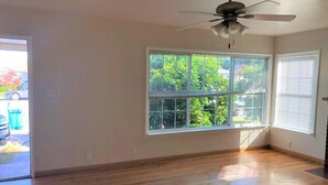 A room with hardwood flooring, a ceiling fan, and a large window with blinds.