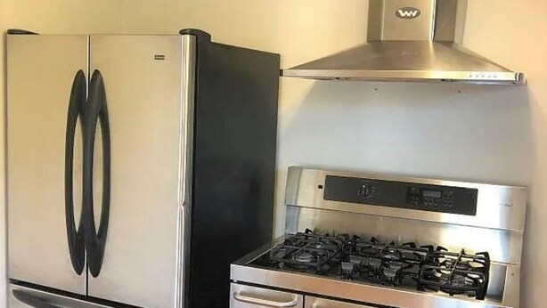 A kitchen with a stainless steel refrigerator, a gas stove, and a range hood.
