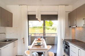 A modern kitchen with a dining area, large windows, and a view of greenery. - Sea View & Luxury Apartment Domania' with Wi-Fi and Air Conditioning (Καληκρατειας Σωζόπολη)