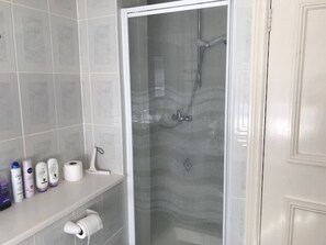 A bathroom with a shower, toilet paper, and toiletries on a shelf. - Kent Apartment 2 bed  in Sandwich, with Free Parking (Sandwich)
