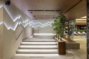 Un espace piscine intérieur moderne, doté d’un jacuzzi, de marches menant à la piscine et de chaises longues.