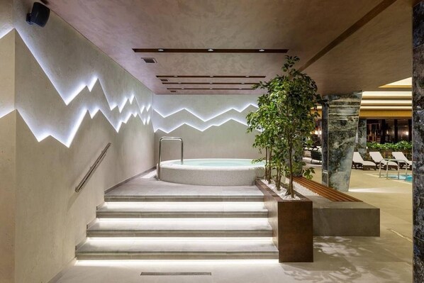 Ein moderner Poolbereich im Innenbereich mit Whirlpool, Treppen zum Pool und Liegestühlen.