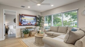 A living room with a beige sofa, a round coffee table, a painting, and a large window with blinds. - Completedly Renovated Pool: Home Minutes to Beach! (North Palm Beach)