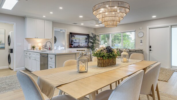A modern kitchen with white cabinets, a wooden dining table, and a chandelier. - Completedly Renovated Pool: Home Minutes to Beach! (North Palm Beach)