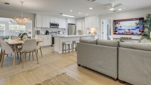 A modern kitchen with white cabinets, a dining area with a wooden table and chairs, and a living area with a grey sofa. - Completedly Renovated Pool: Home Minutes to Beach! (North Palm Beach)