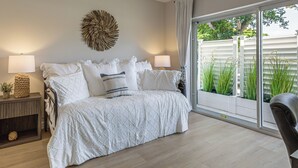 A bedroom with a bed, two bedside tables, a wall decoration, and a view of greenery through a sliding door. - Completedly Renovated Pool: Home Minutes to Beach! (North Palm Beach)