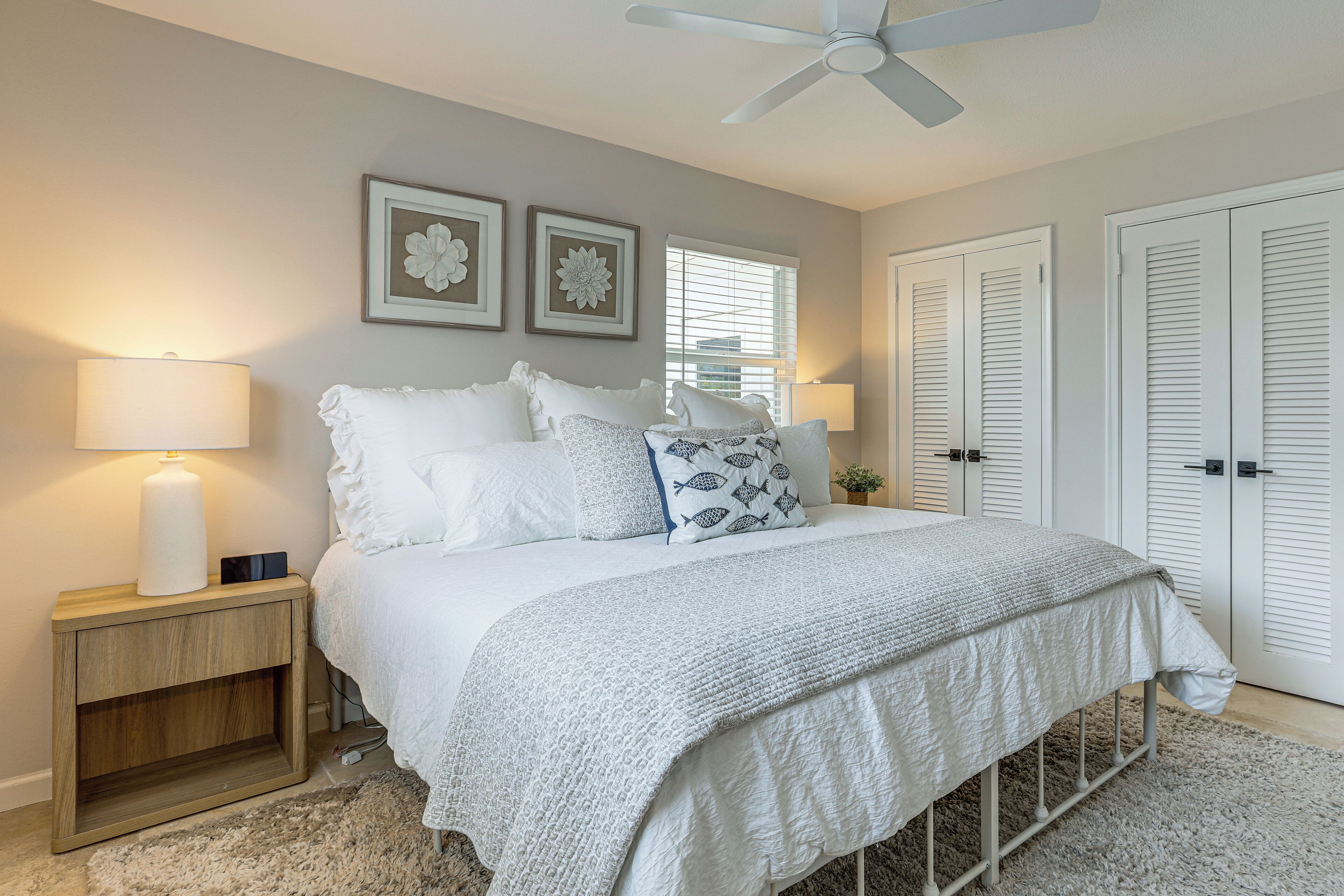 A bedroom with a bed, bedside lamps, a nightstand, a ceiling fan, and two framed pictures on the wall.