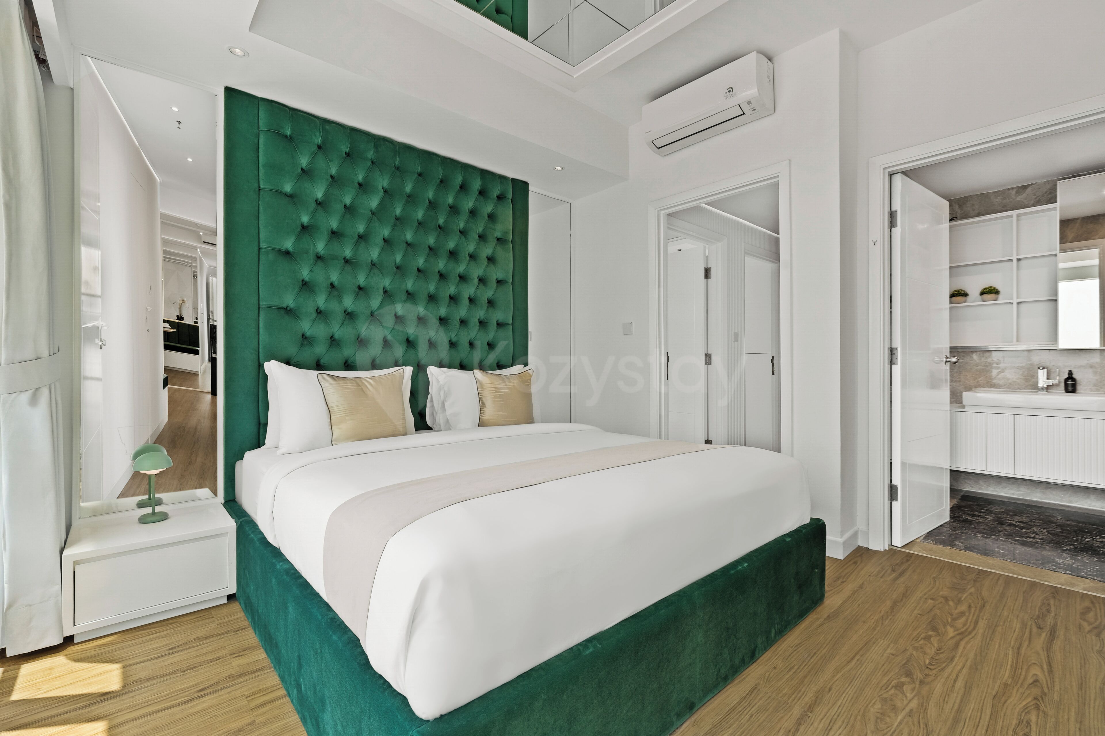 Une chambre à coucher moderne avec une tête de lit verte à motifs capitonnés, une couvre-lit blanche et un plancher en bois.