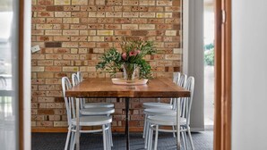 A dining area with a brick wall, a wooden table, and white chairs. - The Palms Sand Dune Middleton (Middleton)
