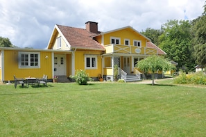 Um edifício amarelo com varanda, escadas e uma pequena árvore na frente.
