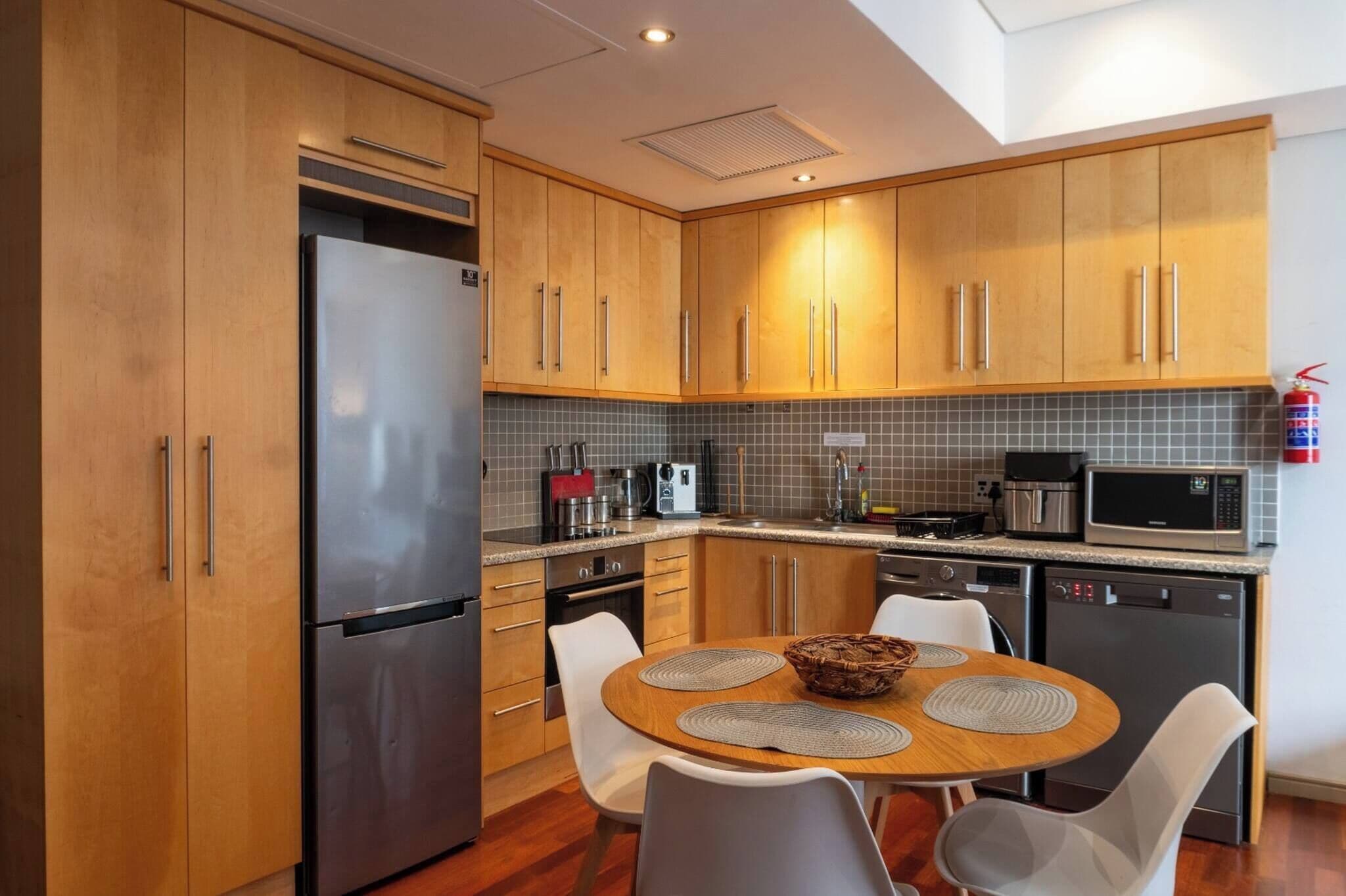A modern kitchen with wooden cabinets, stainless steel appliances, and a dining area with a round table and chairs.