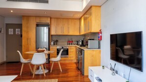Eine moderne Küche mit Holzschränken, Edelstahlgeräten, einem Essbereich mit weißen Stühlen und einem an der Wand befestigten Flachbildfernseher.