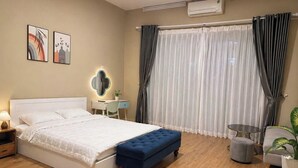 Une chambre à coucher comprenant un lit, une table de chevet, une lampe, une commode, une coiffeuse, un miroir, des rideaux et une plante en pot.