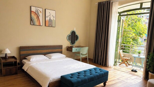 Une chambre d’hôtel comprenant un lit, une table de chevet, une commode, une chaise, une petite table et un balcon avec vue sur la verdure.