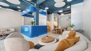 Un área de recepción moderna con un mostrador azul, asientos con cojines e iluminación colgante.